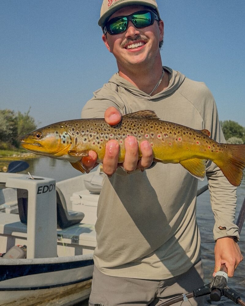 Ben Zell holding a wild brown trout boat-side on a Montana river